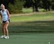 Female golfer putting on the green during a sunny day, showcasing skill and focus on the golf course.