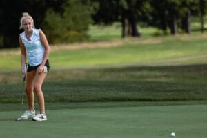 Female golfer putting on the green during a sunny day, showcasing skill and focus on the golf course.