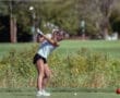 Young girl practicing her golf swing on the course, with balls and flags visible in the background on a sunny day.