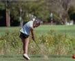 A young golfer swings her club, sending sand flying as she practices her short game on a sunny day.