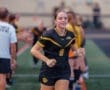 Excited soccer player in black and gold jersey running through teammates' tunnel before the game. Team spirit and energy.