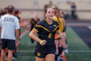Excited soccer player in black and gold jersey running through teammates' tunnel before the game. Team spirit and energy.