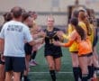Female soccer player walking through a team tunnel, celebrating with teammates before a match on the field.