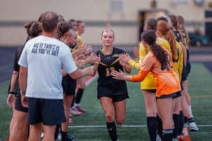 Female soccer player walking through a team tunnel, celebrating with teammates before a match on the field.
