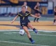 A soccer player in a black jersey kicks the ball on a field during a match, showcasing athleticism and teamwork.