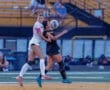 Two female soccer players compete for the ball, showcasing intensity during a match on an outdoor field.