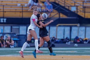 Two female soccer players compete for the ball, showcasing intensity during a match on an outdoor field.
