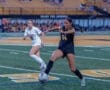 Two female soccer players competing on the field during a match, one in black, the other in white.