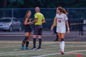 Girls' soccer match with players interacting with the referee on the field during an evening game.
