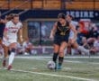 Two female soccer players compete for the ball on a field during an evening match, showcasing athleticism and teamwork.