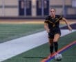 Young female soccer player in a black jersey running on the field with a soccer ball during a game at night.