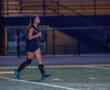 Young female soccer player running on a field at night, showcasing athleticism and focus during a match.