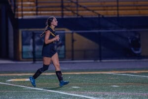 Young female soccer player running on a field at night, showcasing athleticism and focus during a match.