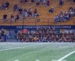 Team huddled on the sidelines during a sports event, with spectators in the background, showcasing school spirit and unity.