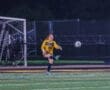 Goalkeeper in yellow uniform kicking the soccer ball during a night game on the field.