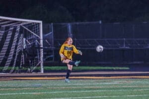 Goalkeeper in yellow uniform kicking the soccer ball during a night game on the field.