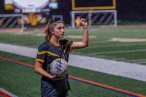 Soccer player signaling while holding a ball on a well-lit field, ready for play during a night match.