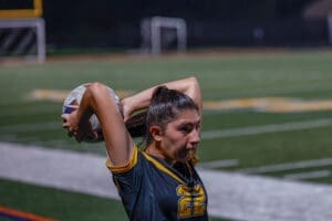 A female soccer player wearing jersey number 22 prepares to throw the ball in a nighttime match on the field.