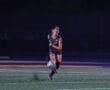Young female soccer player kicking a ball on a field during a night game, showcasing athleticism and skill.