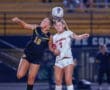 Two female soccer players from competing teams contesting a high ball during an evening match.