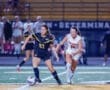 Two female soccer players compete for the ball during a night game on the field, showcasing athleticism and teamwork.