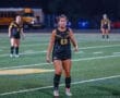 Female soccer player in black uniform with number 23, on field during a night game, focusing on the play ahead.