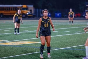 Female soccer player in black uniform with number 23, on field during a night game, focusing on the play ahead.