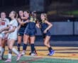 High school girls' soccer players celebrate a goal under stadium lights, showcasing teamwork and sportsmanship.