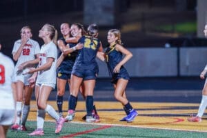 High school girls' soccer players celebrate a goal under stadium lights, showcasing teamwork and sportsmanship.