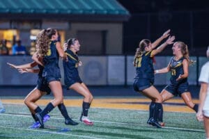 Girls' soccer team celebrates a victory under the stadium lights, showcasing teamwork and joy on the field.