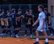 Young soccer players celebrating a goal on the field, wearing black and gold uniforms, with one player in white.