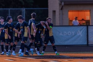 High school soccer team celebrating a goal, showcasing teamwork and camaraderie on the field during a game.