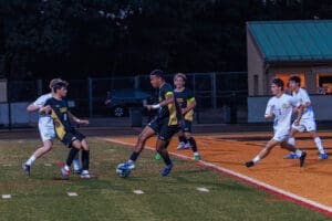 Players compete in a nighttime high school soccer match, showcasing dynamic action on the field.