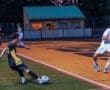 A soccer player in a yellow and black uniform kicks a ball as an opposing player runs nearby during a competitive match.