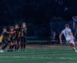 High school soccer players form a wall during a free kick under stadium lights, showcasing team strategy in action.