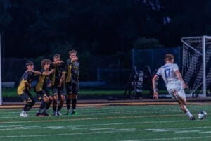 High school soccer players form a wall during a free kick under stadium lights, showcasing team strategy in action.