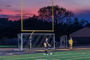 Two young soccer players on a field at dusk, with a colorful sunset and goalposts in the background.