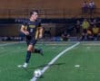 High school soccer player runs with the ball during a night game, showcasing athleticism and teamwork on the field.