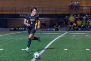 High school soccer player runs with the ball during a night game, showcasing athleticism and teamwork on the field.
