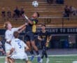 High school soccer match: players compete for the ball in mid-air under stadium lights, capturing an intense moment.