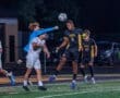 High school soccer players compete for the ball under stadium lights, showcasing action and athleticism on the field.