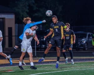 High school soccer players compete for the ball under stadium lights, showcasing action and athleticism on the field.