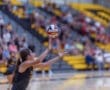 A volleyball player prepares to serve the ball in front of a cheering crowd in a sports arena.