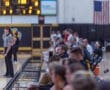Spectators watch a basketball game with a referee in focus and an American flag in the background.