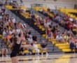 A volleyball player serves the ball in front of an enthusiastic crowd in a gymnasium.