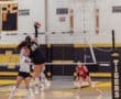 Volleyball players competing at a high school match; player 25 jumps to spike the ball over the net.