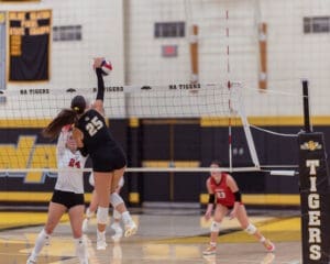 Volleyball players competing at a high school match; player 25 jumps to spike the ball over the net.