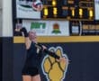 Volleyball player serves the ball during a game, displaying focused determination against the scoreboard backdrop.