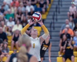 Volleyball player sets the ball in front of a cheering crowd during a competitive match in a vibrant gymnasium.