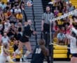 Volleyball player leaps to spike the ball over the net, with spectators watching eagerly in a vibrant gym setting.